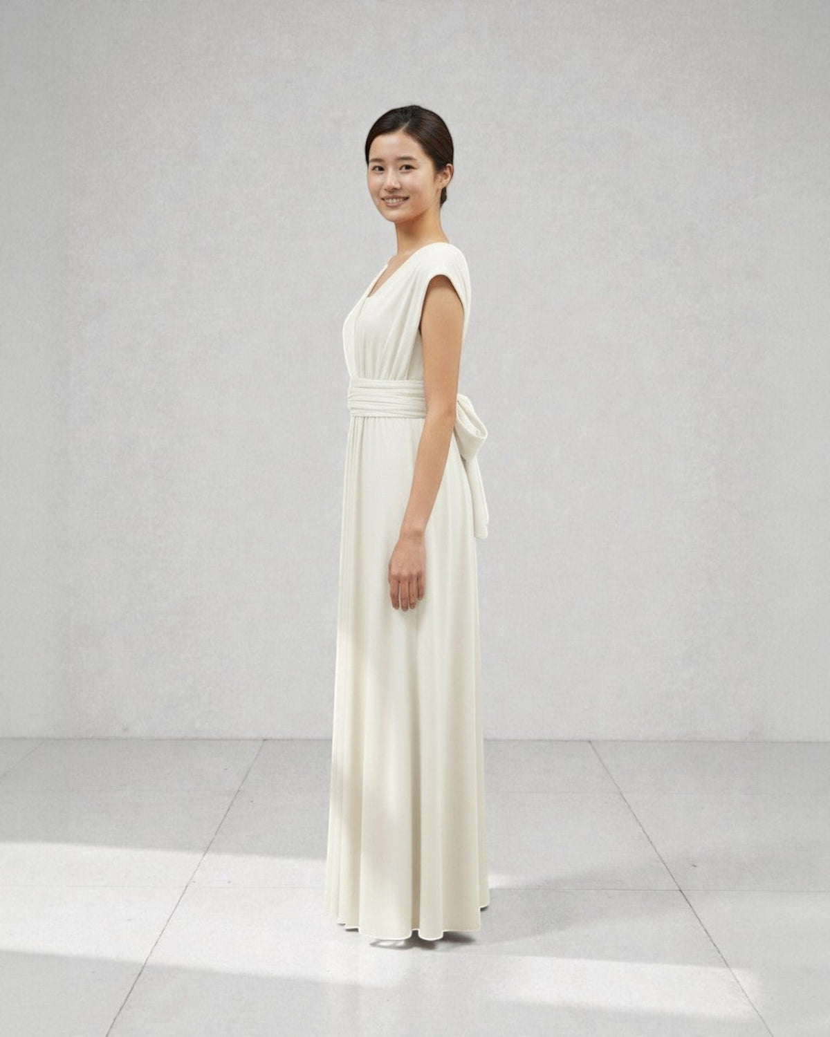 BridesmaidsJP ivory white infinity dress with a sash tied in a bow at the back, worn by a model in a studio.