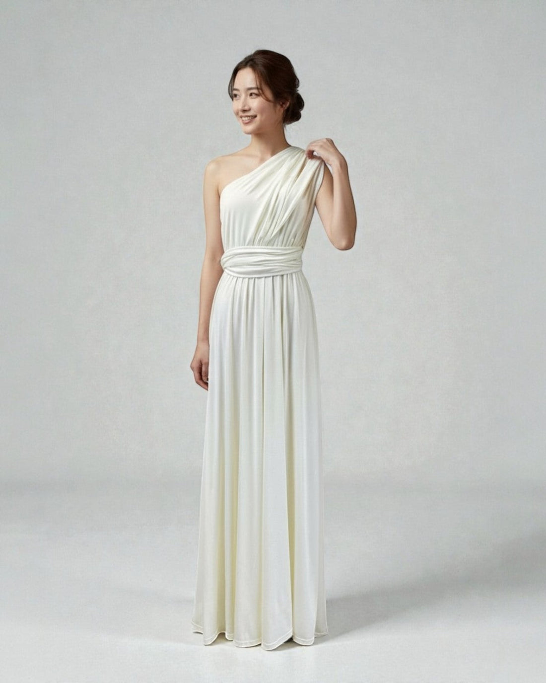 BridesmaidsJP ivory infinity dress styled as a one-shoulder gown on a smiling model against a light grey backdrop.